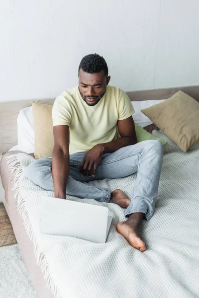 Barefoot african american man typing on laptop in bedroom — Stock Photo