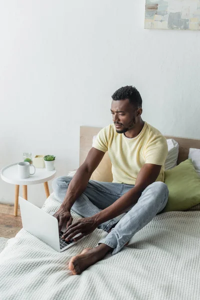 Barefoot african american freelancer typing on laptop in bedroom — Stock Photo