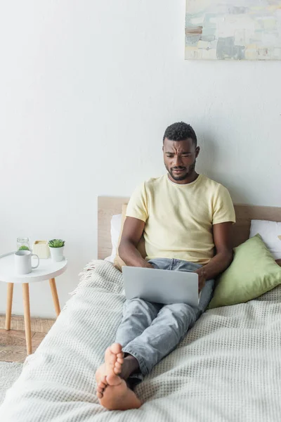 Focused african american freelancer typing on laptop in bedroom — Stock Photo