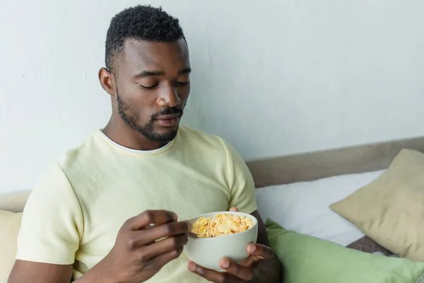 Barbudo hombre afroamericano mirando copos de maíz en tazón - foto de stock