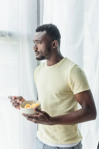 African american man holding spoon and bowl with corn flakes — Stock Photo