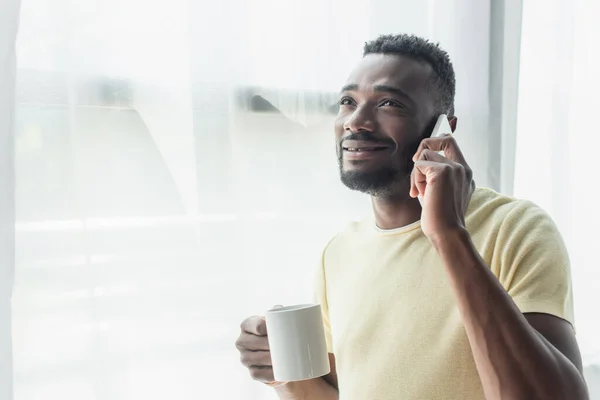 Souriant homme afro-américain tenant tasse avec du thé et parlant sur téléphone portable — Photo de stock