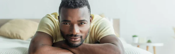 Bärtiger afrikanisch-amerikanischer Mann im T-Shirt auf dem Bett liegend, Banner — Stockfoto