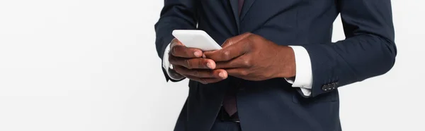 Vista recortada del hombre de negocios afroamericano en traje de mensajería en el teléfono inteligente aislado en gris, bandera - foto de stock