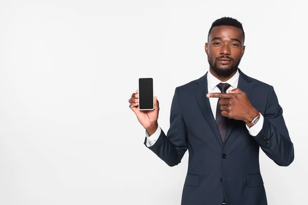 African american businessman in suit pointing at smartphone with blank screen isolated on grey — Stock Photo