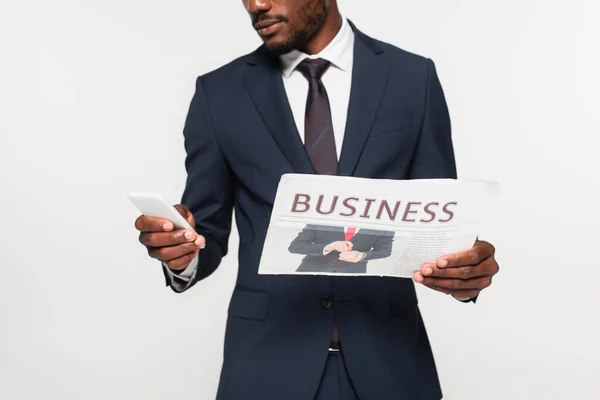 Vista recortada del hombre afroamericano en traje usando teléfono inteligente mientras mantiene periódico de negocios aislado en gris - foto de stock