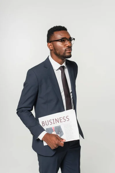 Homem americano africano em óculos segurando jornal de negócios isolado em cinza — Fotografia de Stock