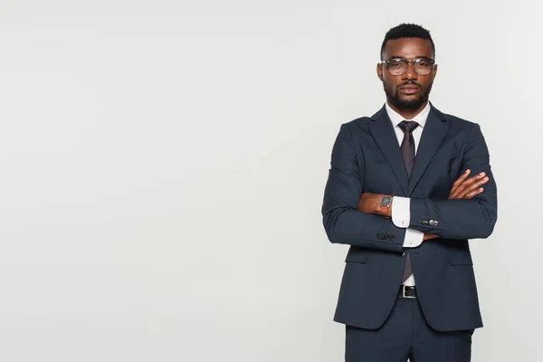 Hombre afroamericano en gafas de pie con brazos cruzados aislados en gris - foto de stock