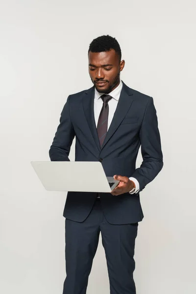 African american businessman in suit using laptop isolated on grey — Stock Photo