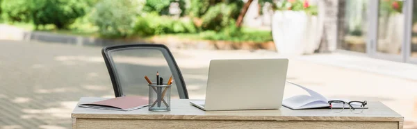 Ноутбук рядом ноутбук и канцелярские принадлежности на столе снаружи, баннер — стоковое фото