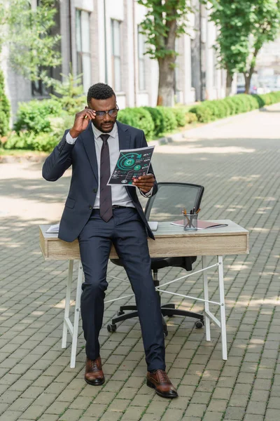 In voller Länge afrikanisch-amerikanischer Geschäftsmann mit Brille beim Betrachten gedruckter Infografiken — Stockfoto