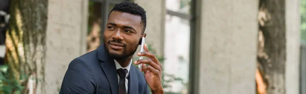 Barbudo hombre de negocios afroamericano hablando por teléfono móvil afuera, pancarta - foto de stock