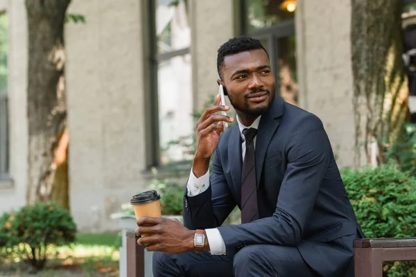 Bearded african american businessman talking on mobile phone and holding coffee to go outside — Stock Photo