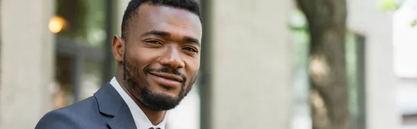 Sonriente hombre de negocios afroamericano en traje mirando a la cámara exterior, pancarta - foto de stock