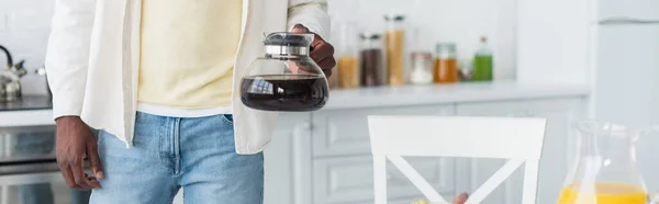 Cropped view of african american man holding coffee pot in kitchen, banner — Stock Photo