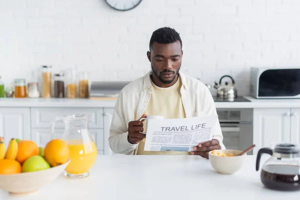 Barbudo hombre afroamericano sosteniendo taza de café y leyendo el periódico de viaje de la vida - foto de stock