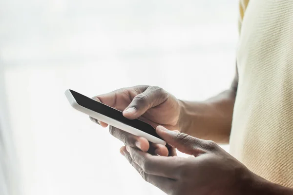 Vista recortada del hombre afroamericano mensajes de texto en el teléfono inteligente - foto de stock