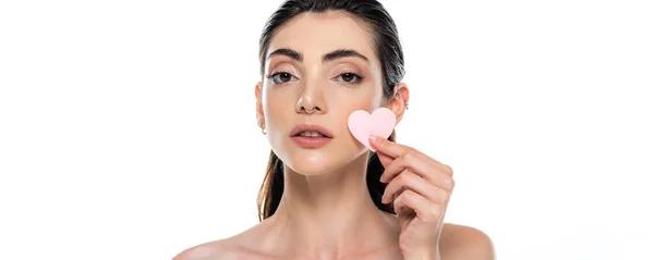 Pierced young woman with bare shoulders holding heart-shape sponge isolated on white, banner — Stock Photo
