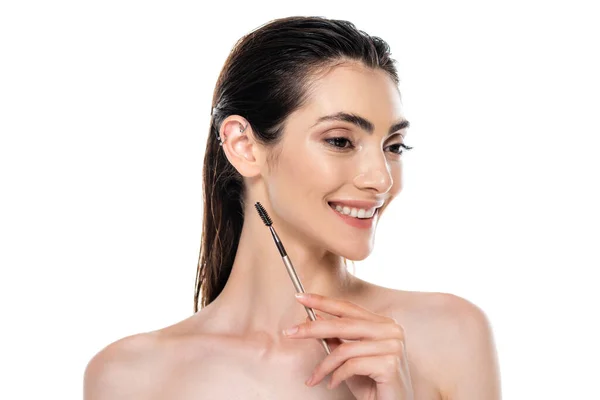 Smiling young woman with bare shoulders holding eyebrow brush isolated on white — Stock Photo