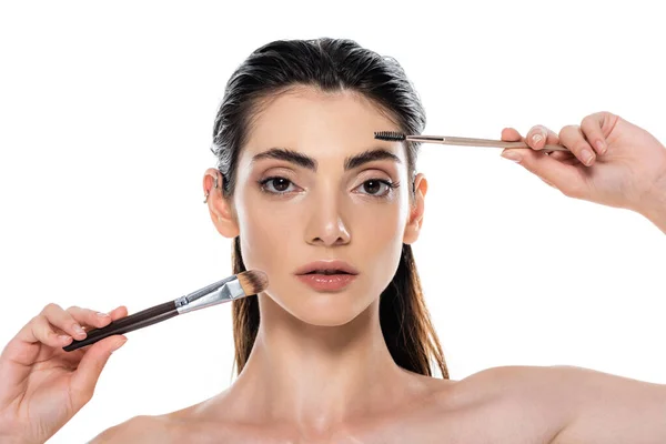 Mujer joven con hombros desnudos sosteniendo cejas y cepillos cosméticos aislados en blanco — Stock Photo