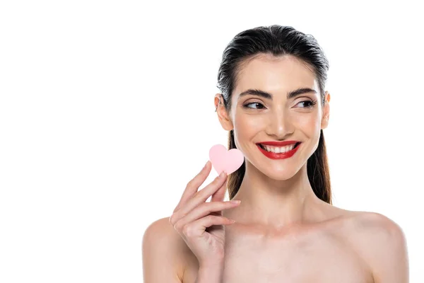 Positive Frau mit roten Lippen hält herzförmigen Schönheitsschwamm isoliert auf weiß — Stockfoto