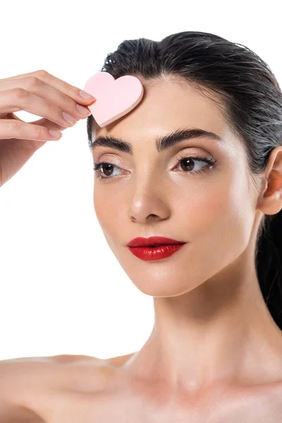 Brünette Frau mit roten Lippen hält herzförmigen Schönheitsschwamm isoliert auf weiß — Stockfoto