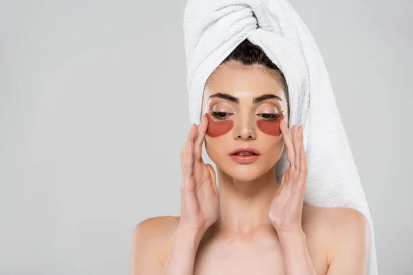 Jeune femme avec serviette sur la tête appliquant des patchs pour les yeux isolés sur gris — Photo de stock