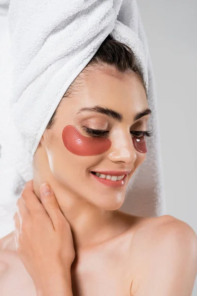 Cheerful young woman with towel on head and eye patches isolated on grey — Stock Photo