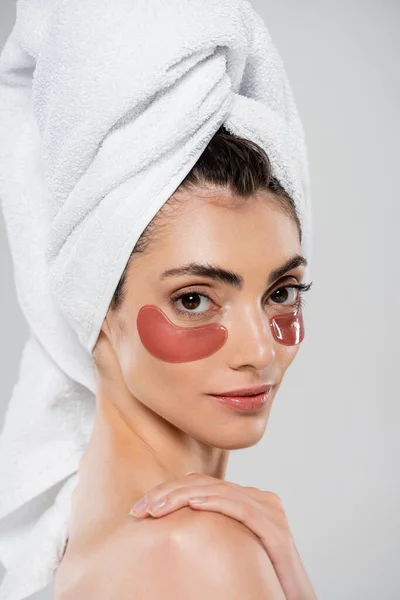 Jolie jeune femme avec serviette sur la tête et les yeux patchs isolés sur gris — Photo de stock