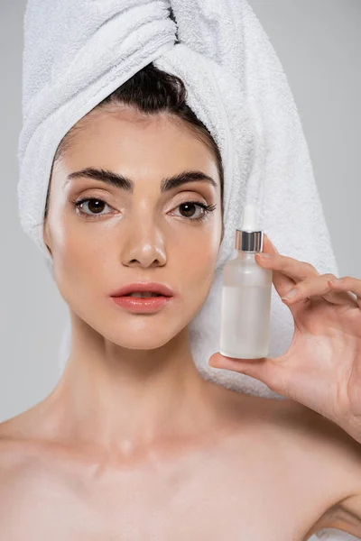 Junge Frau mit Handtuch auf dem Kopf hält Flasche mit Serum isoliert auf grau — Stockfoto