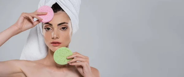 Jovem com toalha na cabeça segurando esponjas de beleza isoladas em cinza, banner — Fotografia de Stock