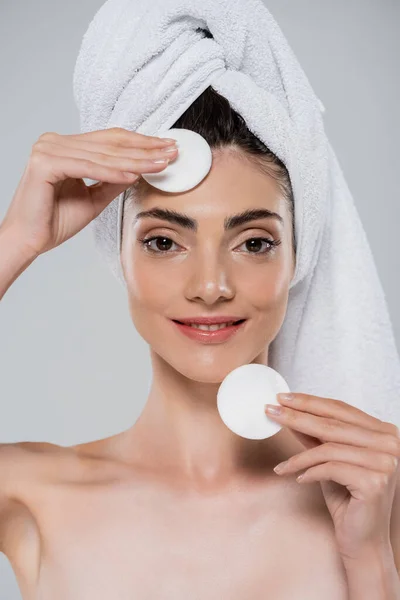 Femme souriante avec serviette sur la tête démaquillage avec des tampons de coton isolés sur gris — Photo de stock