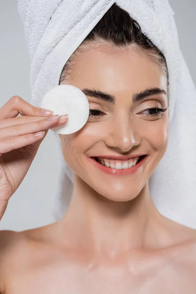 Cheerful young woman with towel holding cotton pad isolated on grey — Stock Photo