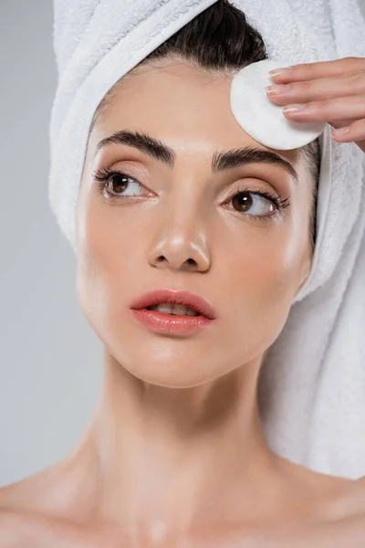 Mujer con toalla en la cabeza quitando maquillaje con almohadilla de algodón aislado en gris - foto de stock