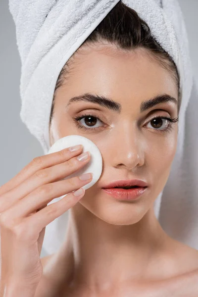 Young woman with towel on head applying tonic with cotton pad isolated on grey — Stock Photo