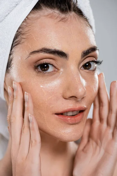 Young woman with towel on head washing face and removing foundation isolated on grey — Stock Photo