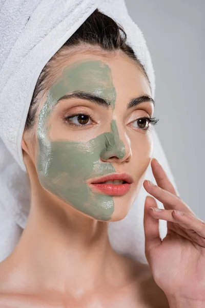 Jeune femme avec serviette sur la tête et masque en argile verte sur le visage isolé sur gris — Photo de stock