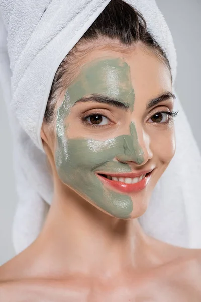 Allegra giovane donna con asciugamano sulla testa e maschera di argilla verde sul viso isolato su grigio — Foto stock