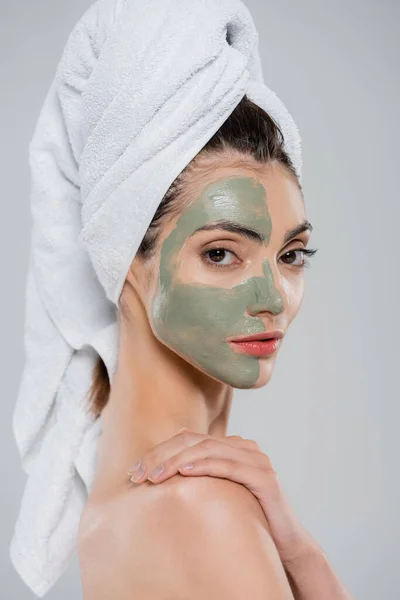 Jeune femme avec serviette sur la tête et masque en argile sur le visage isolé sur gris — Photo de stock