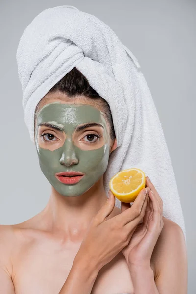 Junge Frau mit grüner Lehmmaske, die reife Orange halb isoliert auf grau hält — Stockfoto