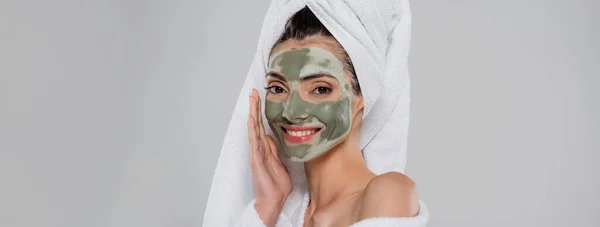 Happy young woman with towel on head and clay mask on face looking at camera isolated on grey, banner — Stock Photo