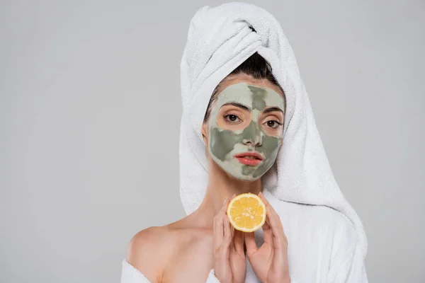 Jeune femme avec masque en argile verte tenant orange à moitié isolé sur gris — Photo de stock