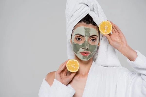 Jovem mulher com máscara de barro verde segurando metades maduras de laranja isolada em cinza — Fotografia de Stock