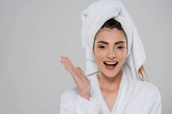 Stupita giovane donna in accappatoio con asciugamano sulla testa isolato su grigio — Foto stock