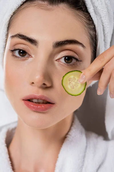 Close up of young woman with towel on head applying sliced cucumber on face isolated on grey — Stock Photo