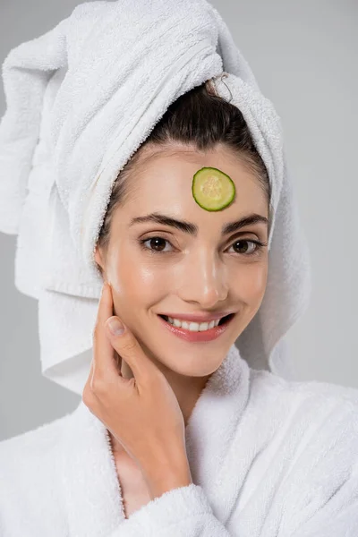 Happy young woman with towel on head and sliced cucumber on face isolated on grey — Stock Photo