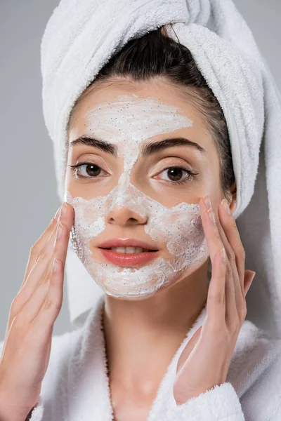 Jeune femme avec serviette sur la tête appliquer gommage visage isolé sur gris — Photo de stock