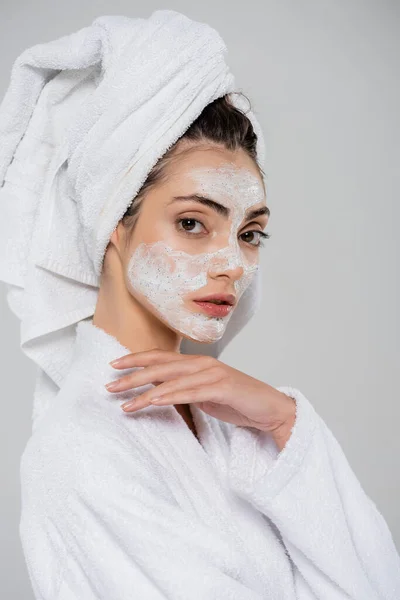 Mujer bonita con toalla en la cabeza y exfoliante facial aislado en gris - foto de stock