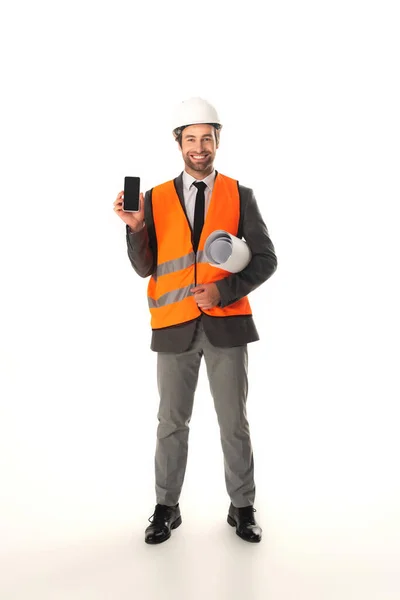Ingeniero sonriente sosteniendo smartphone y plano sobre fondo blanco - foto de stock