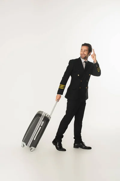 Pilote souriant avec valise pointant du doigt sur fond blanc — Photo de stock